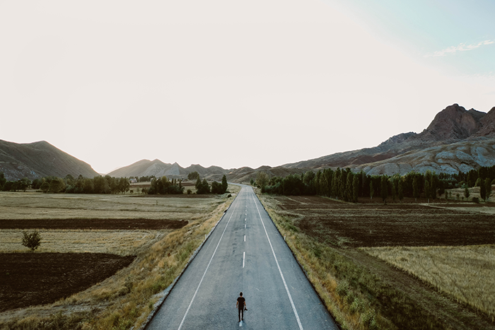 person standing in the middle of a long road 
